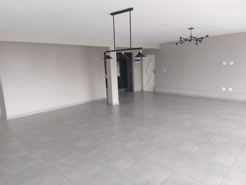Spacious open-plan living area featuring large format grey floor tiles, modern pendant lighting, and neutral wall finishes in a clean, vacant space.