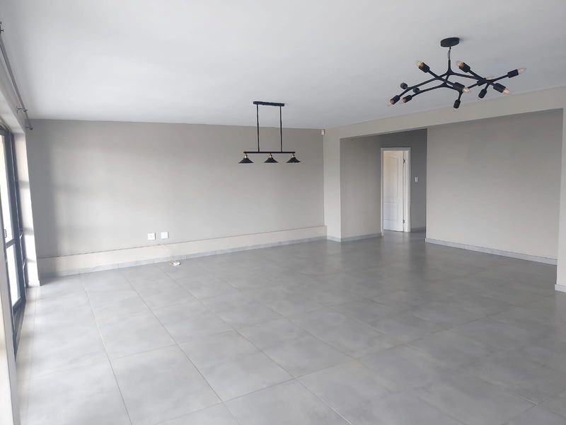 A spacious, open-plan living area featuring neutral grey floor tiles, modern pendant lighting, and large sliding glass doors providing ample natural light.
