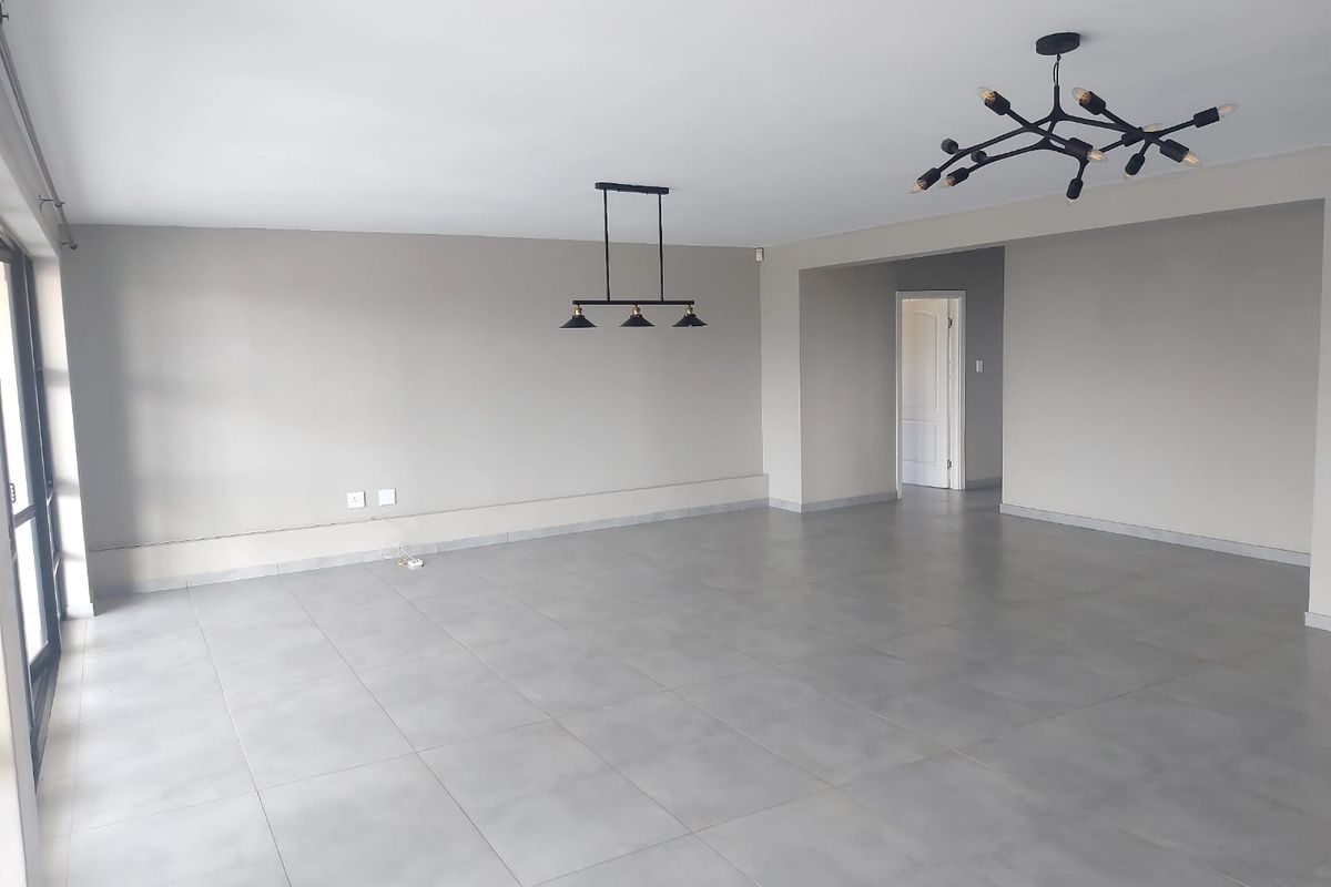 A spacious, open-plan living area featuring neutral grey floor tiles, modern pendant lighting, and large sliding glass doors providing ample natural light.