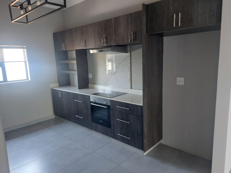 Modern kitchen featuring dark wood cabinetry, stone countertops, integrated electric hob and oven, and sleek tiled flooring in a clean, contemporary space.