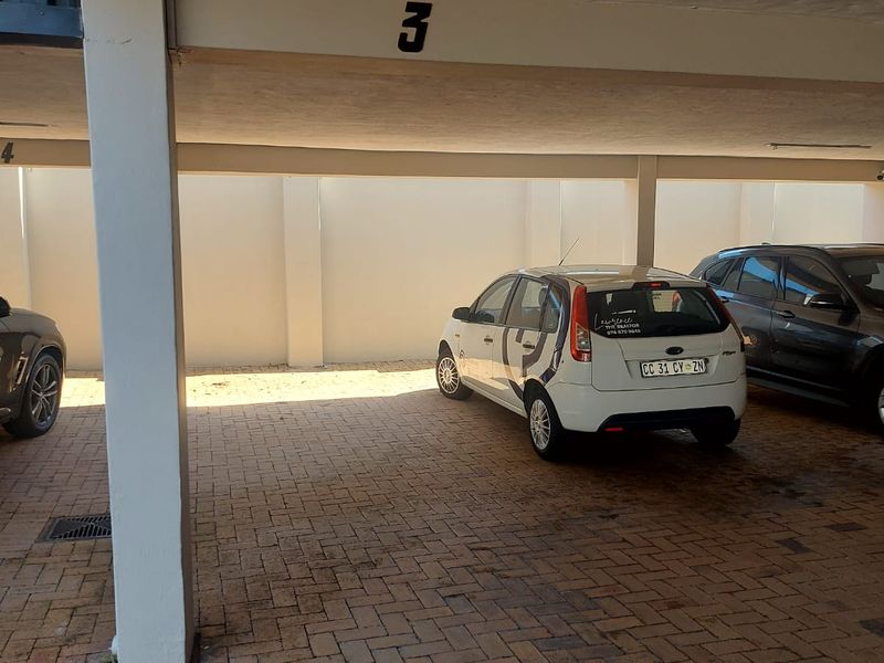 A covered parking bay featuring paved flooring and concrete structural supports within an apartment complex.