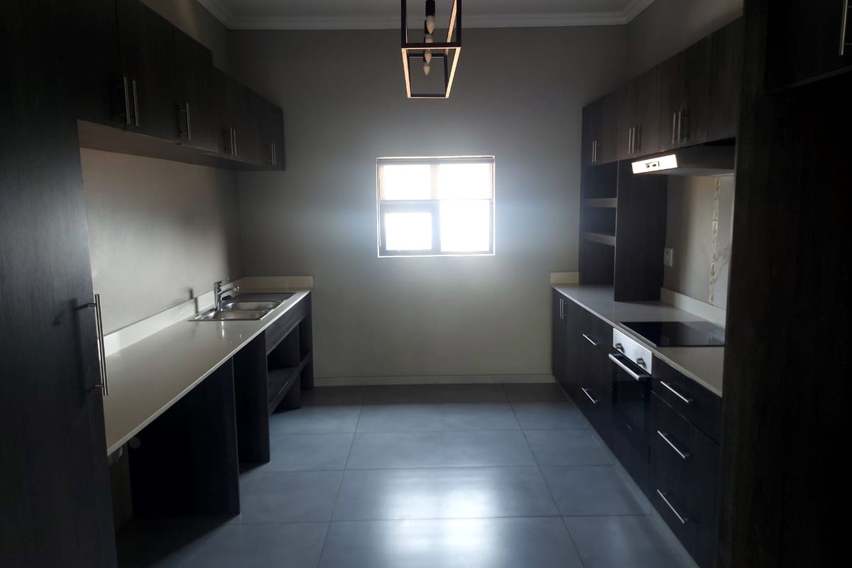 Modern kitchen featuring dark cabinetry, stone countertops, integrated oven and hob, and large format floor tiles in a clean, contemporary layout.