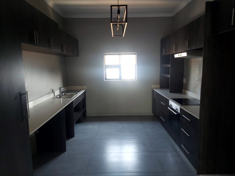 Modern kitchen featuring dark cabinetry, stone countertops, integrated oven and hob, and large format floor tiles in a clean, contemporary layout.