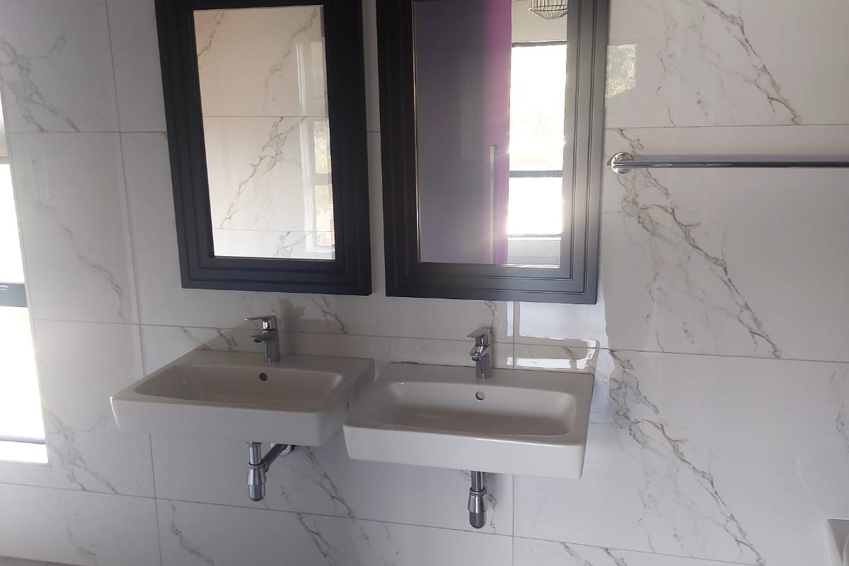 Modern bathroom featuring double wall-mounted basins with chrome fixtures, elegant marble-look wall tiling, and large format floor tiles.