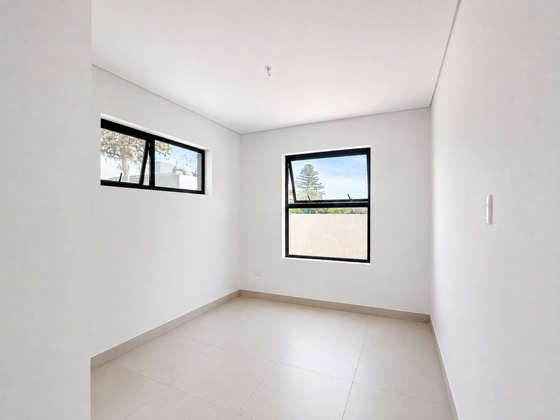 A bright, empty bedroom featuring neutral tiled flooring and modern black aluminium window frames, offering a clean and versatile space.