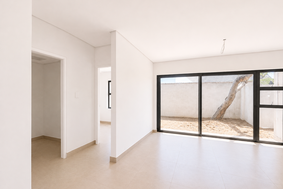 A bright, modern, and empty living area featuring neutral tiled flooring and large sliding glass doors that open to a private rear courtyard.