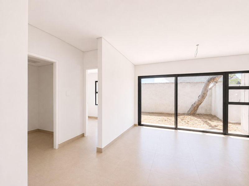 A bright, modern, and empty living area featuring neutral tiled flooring and large sliding glass doors that open to a private rear courtyard.