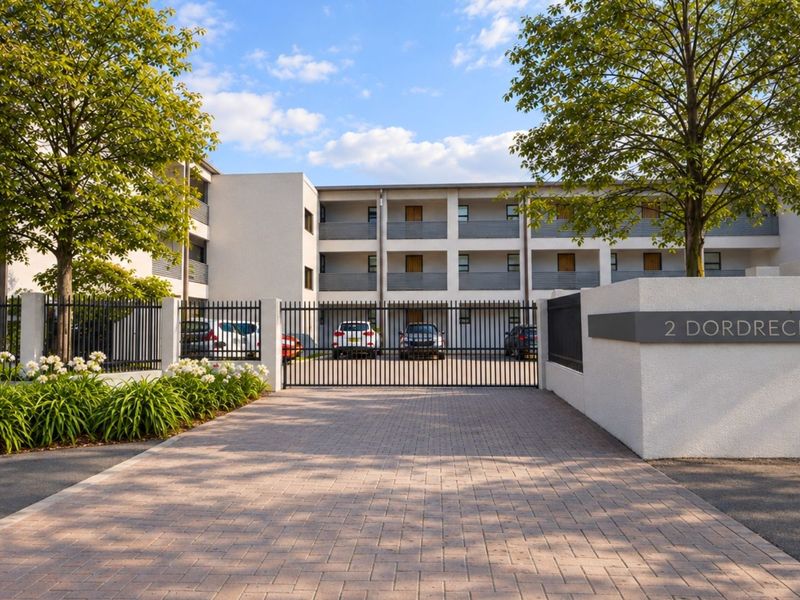 Front view of a modern apartment complex featuring a secure gated entrance, paved driveway, and well-maintained building facade with balconies.
