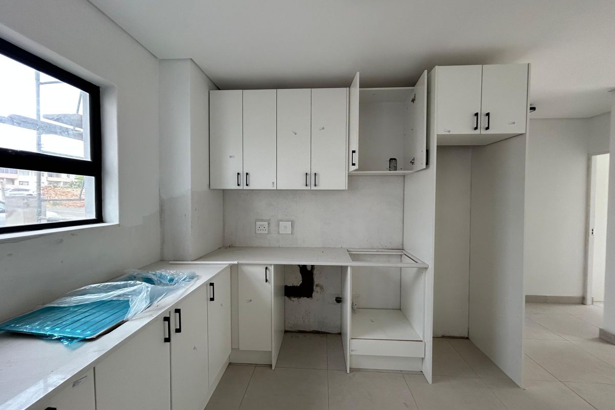 An unfinished kitchen space featuring white cabinetry, tiled flooring, and a sink, requiring final touches and appliance installation to complete the functional area.