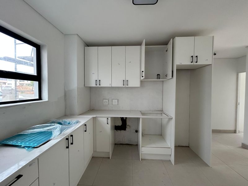 An unfinished kitchen space featuring white cabinetry, tiled flooring, and a sink, requiring final touches and appliance installation to complete the functional area.