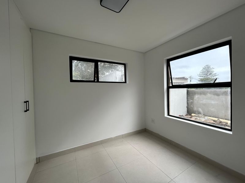 A bright, empty bedroom featuring neutral tiled flooring, built-in cupboards, and modern aluminium-framed windows.