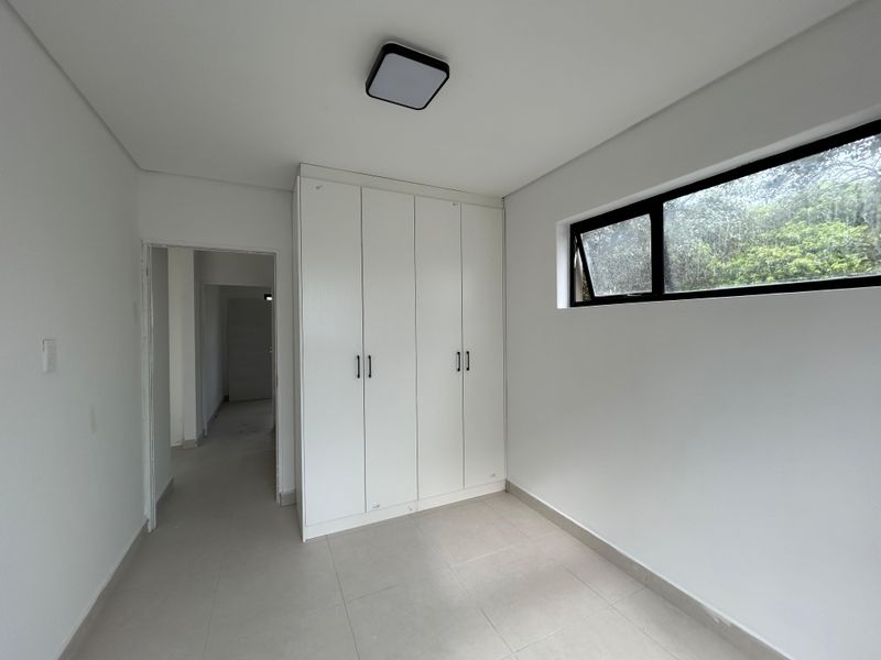 A bright, empty bedroom featuring neutral tiled flooring, a built-in wardrobe, and a modern aluminium-framed window.