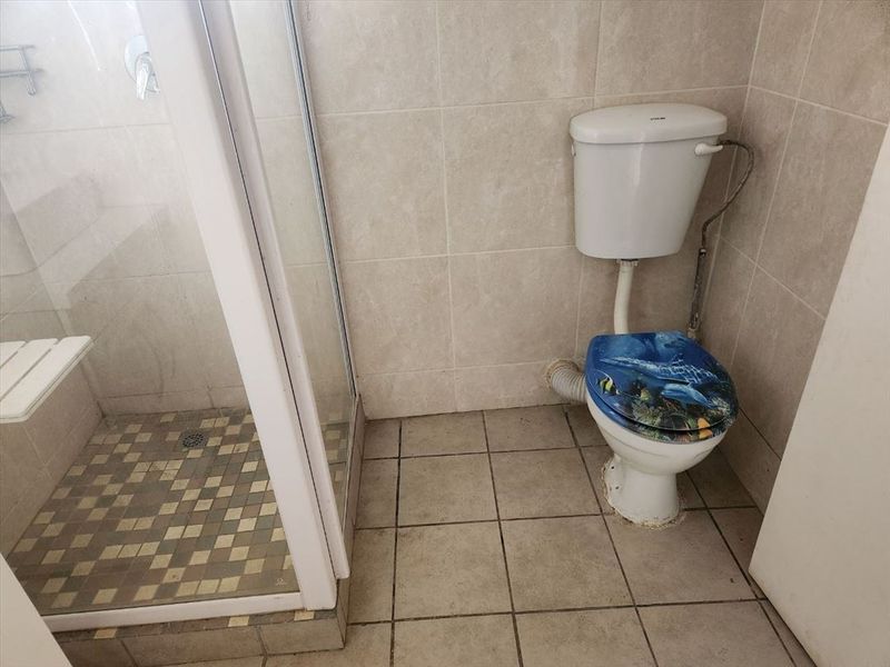 A functional bathroom featuring a shower enclosure and toilet with tiled walls and flooring, requiring cosmetic updates to improve its overall condition.