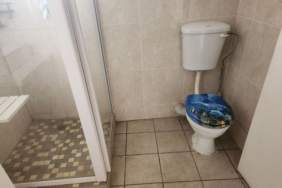 A functional bathroom featuring a shower enclosure and toilet with tiled walls and flooring, requiring cosmetic updates to improve its overall condition.
