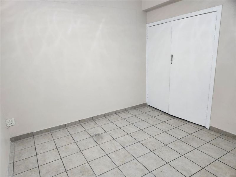 An empty bedroom featuring neutral tiled flooring and a built-in cupboard, providing a blank canvas for personalization.