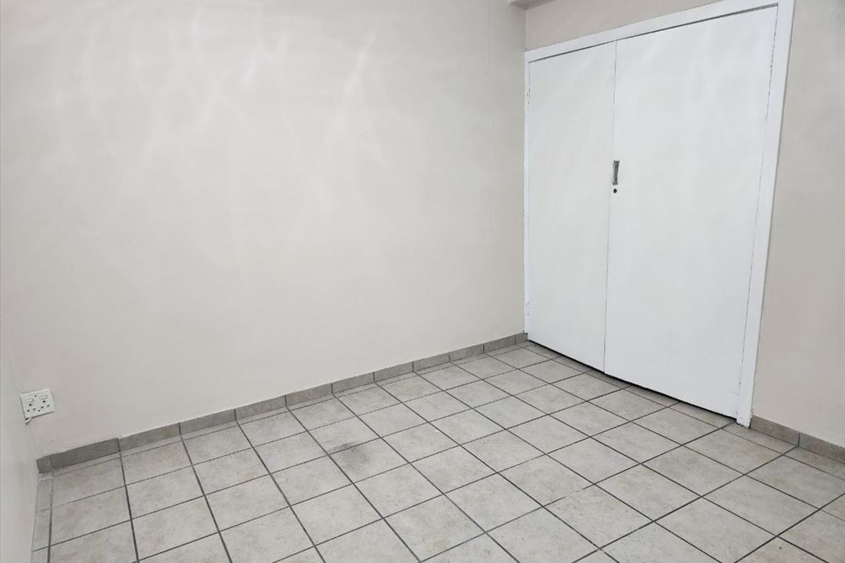 An empty bedroom featuring neutral tiled flooring and a built-in cupboard, providing a blank canvas for personalization.