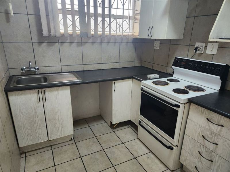 A functional kitchen featuring tiled walls and floors, laminate countertops, a stainless steel sink, and a freestanding electric stove.