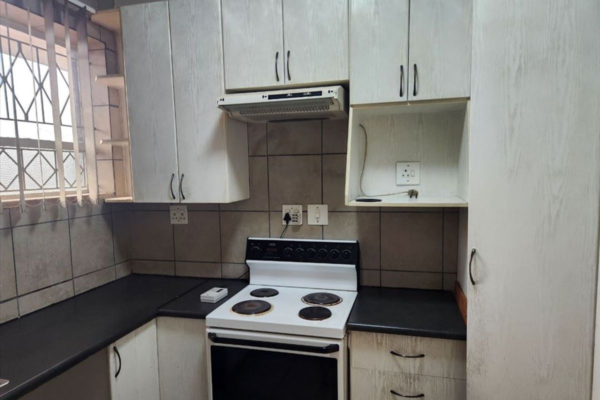 A functional kitchen featuring built-in cabinetry, a tiled backsplash, and a freestanding electric stove with an integrated extractor fan.