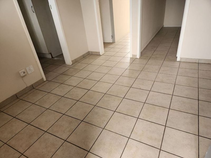 A vacant hallway featuring neutral ceramic floor tiles and multiple doorways leading to adjacent rooms, presenting a clean and functional transition space.