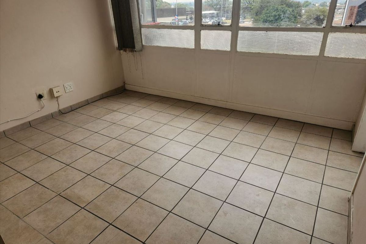 An empty living area featuring tiled flooring and large windows with natural light, offering a blank canvas for renovation or staging.