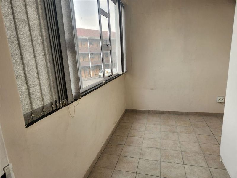 An empty bedroom featuring tiled flooring, vertical blinds, and an aluminium window frame, requiring minor cosmetic updates to the wall finishes.