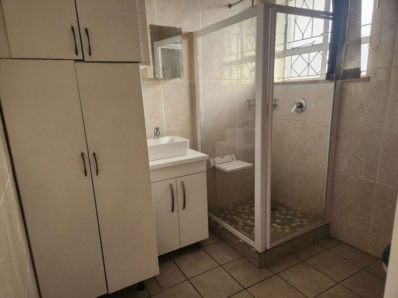 A functional bathroom featuring a shower enclosure, vessel sink with vanity cabinet, and additional built-in storage cupboards with tiled walls and floors.