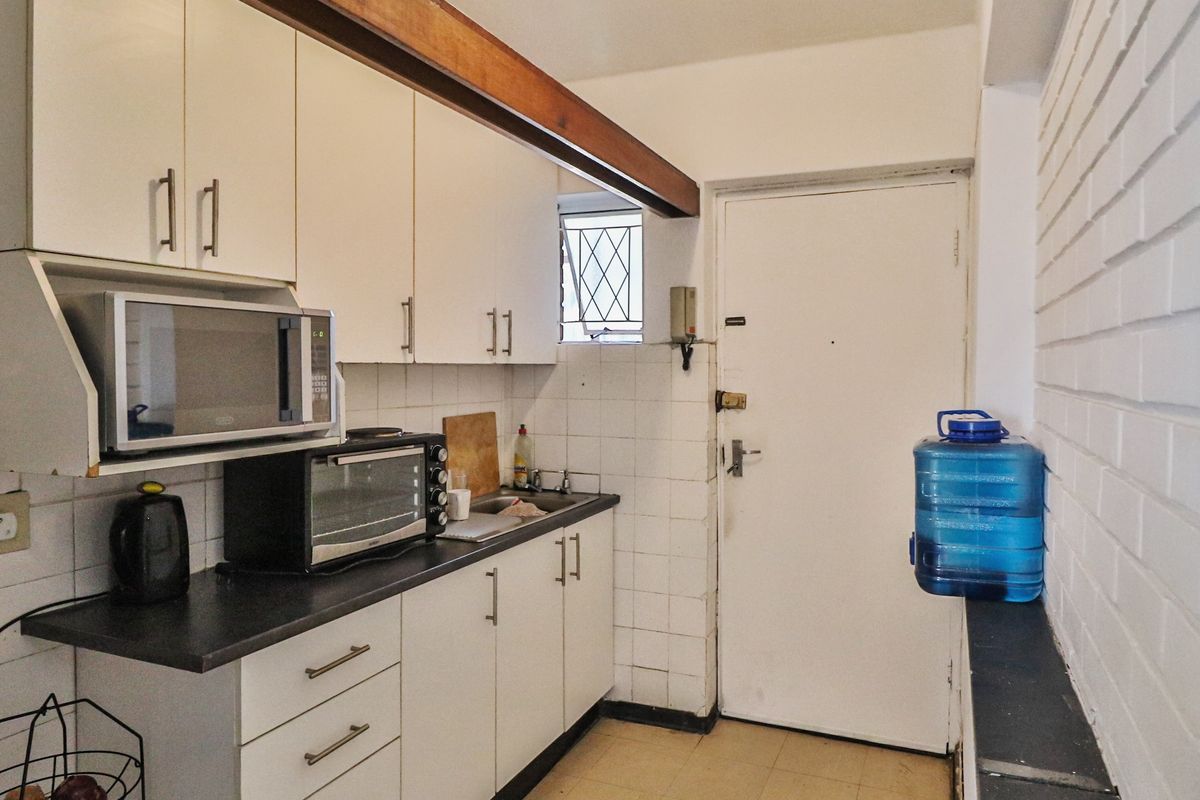 Compact kitchen featuring white cabinetry, dark laminate countertops, tiled backsplash, and an exposed timber beam, providing a functional but dated culinary workspace.