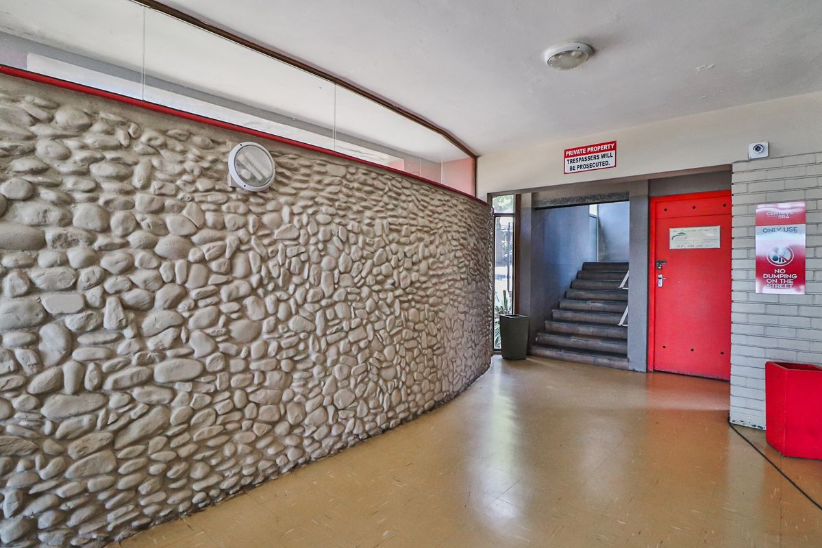 A communal apartment building entrance featuring a curved stone-clad feature wall, vinyl flooring, and access to a staircase.