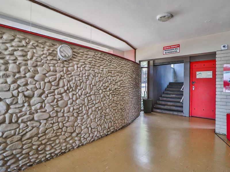 A communal apartment building entrance featuring a curved stone-clad feature wall, vinyl flooring, and access to a staircase.