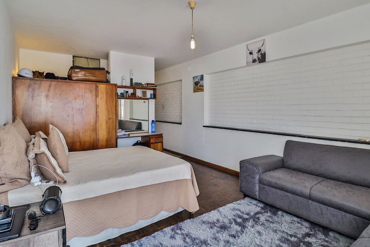 Spacious bedroom featuring parquet flooring, a built-in wardrobe with integrated vanity, and a decorative exposed brick wall.