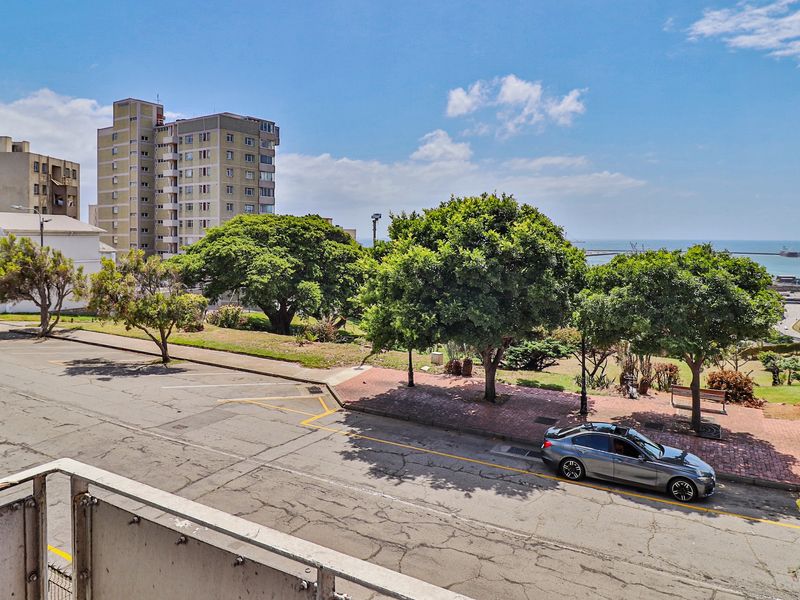 An elevated view overlooking a street, public park area, and the distant ocean horizon from a balcony.