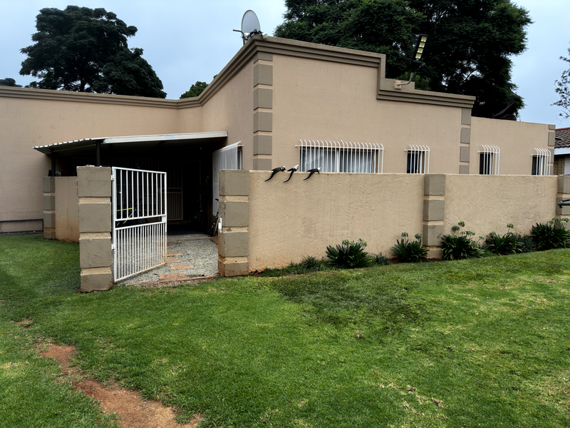 Front exterior view of a single-story house featuring a boundary wall, security bars on windows, and a gated entrance with a paved walkway.