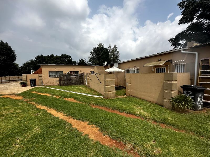 Rear exterior view of the property featuring a lawn area, boundary walls with security bars, and a paved driveway section.