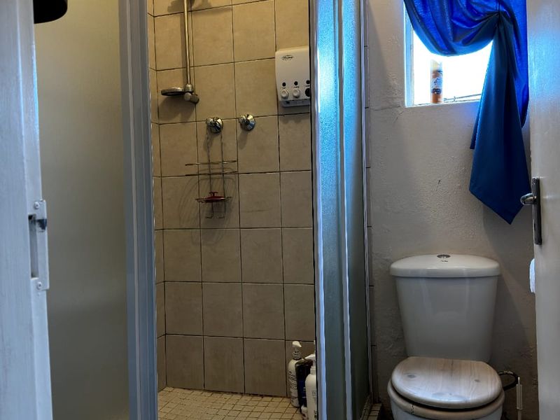 A compact bathroom featuring a shower enclosure with tiled walls and a standard toilet, requiring some maintenance and cosmetic updates.