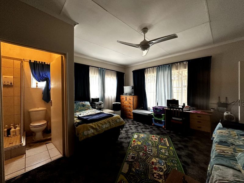 A bedroom featuring an en-suite bathroom with a shower and toilet, equipped with a ceiling fan and carpeted flooring.
