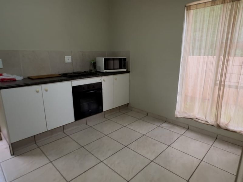 A compact kitchen featuring built-in cabinetry, a gas hob, an oven, and tiled flooring, with direct access to an outdoor area.