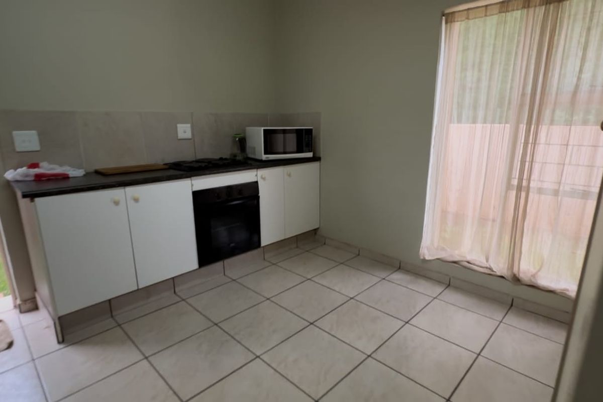 A compact kitchen featuring built-in cabinetry, a gas hob, an oven, and tiled flooring, with direct access to an outdoor area.