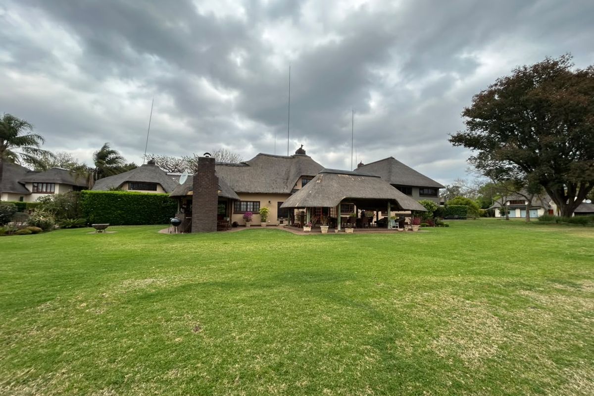 Rear view of a spacious property featuring a large manicured lawn, a thatched roof structure, and a covered outdoor entertainment patio area.