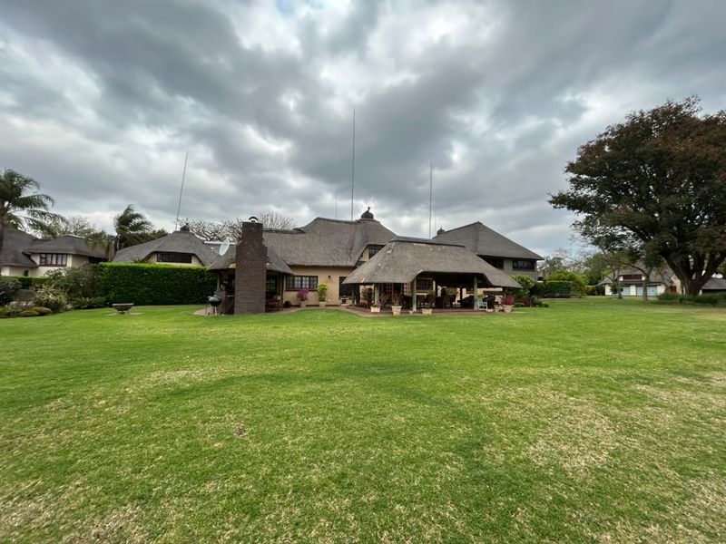 Rear view of a spacious property featuring a large manicured lawn, a thatched roof structure, and a covered outdoor entertainment patio area.