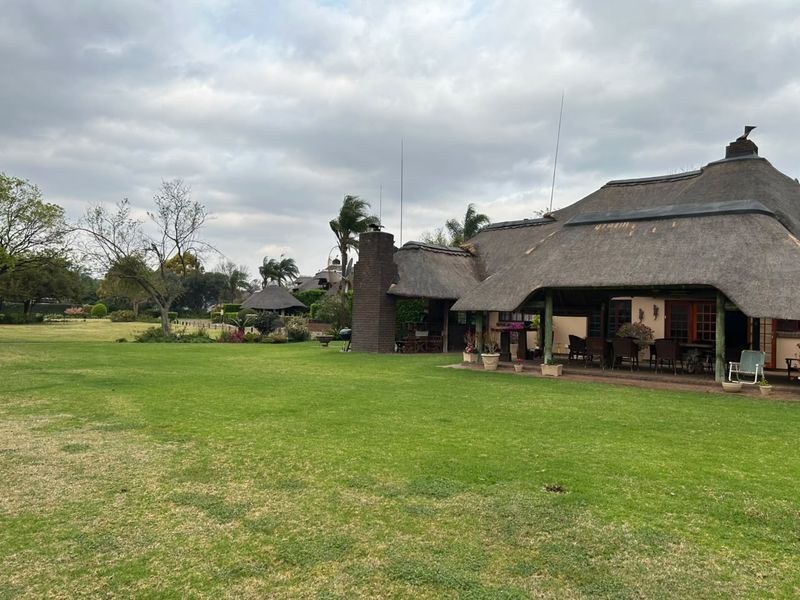 Spacious rear garden featuring a large lawn and a covered patio area with a traditional thatched roof and brick chimney.