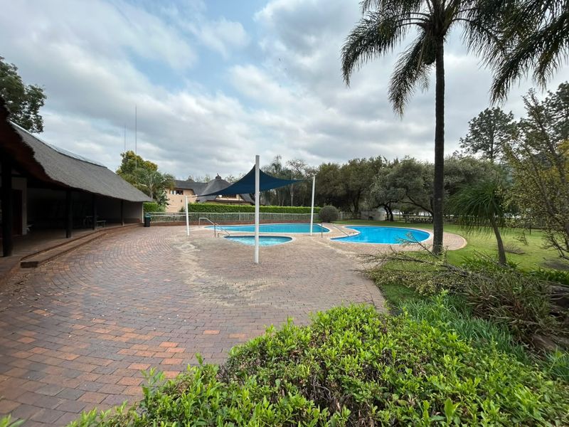 Outdoor pool area featuring a paved patio, swimming pool with shade sail, and a covered thatch roof structure.