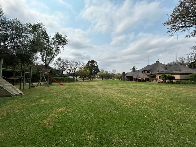 Expansive, well-maintained garden featuring a large lawn, mature trees, and a view of the main residence with a traditional thatched roof.