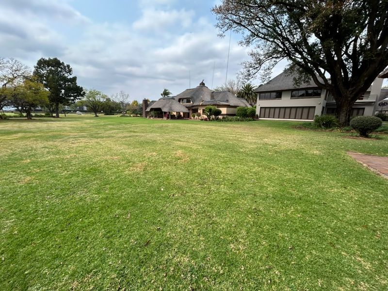 A spacious, well-maintained garden featuring a large lawn and mature trees, providing a clear view of the thatched-roof residence.