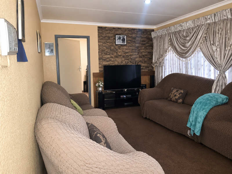 A comfortable living room featuring a brick-effect accent wall, neutral wall tones, and carpeted flooring, providing a cozy space for relaxation.