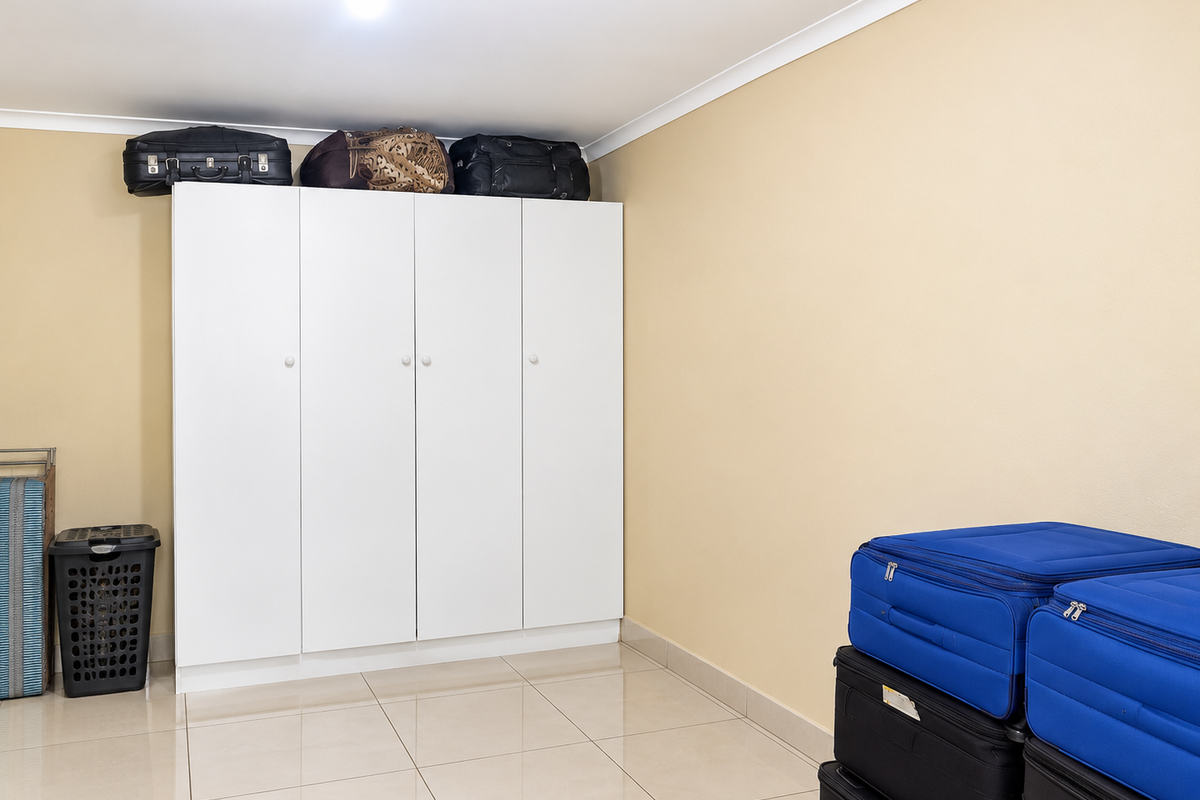 A bedroom featuring neutral walls, tiled flooring, and a white built-in wardrobe providing ample storage space.