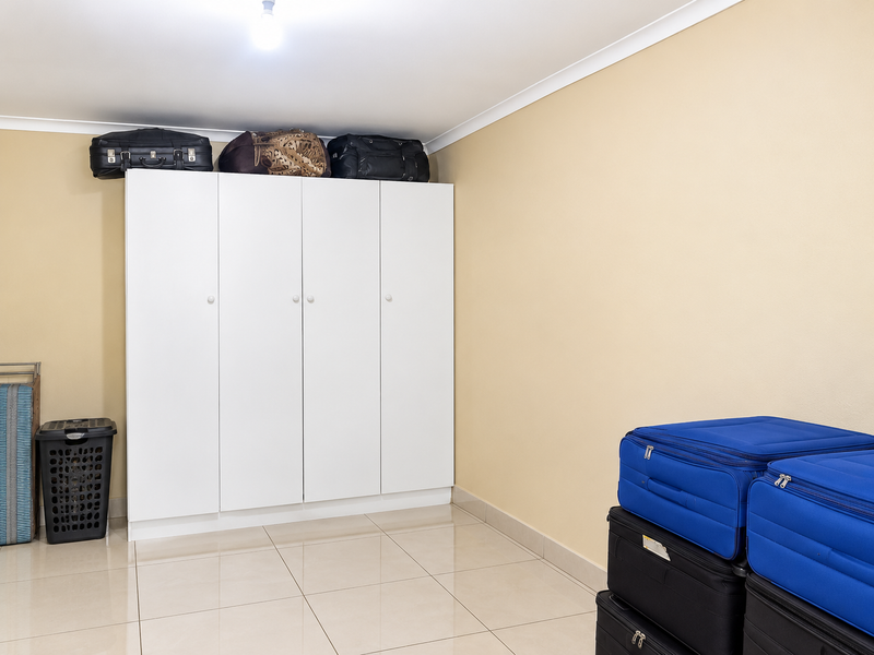 A bedroom featuring neutral walls, tiled flooring, and a white built-in wardrobe providing ample storage space.
