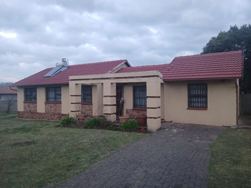 Front view of a single-story house featuring a tiled roof, solar water heater, and a paved driveway with security features on windows and doors.