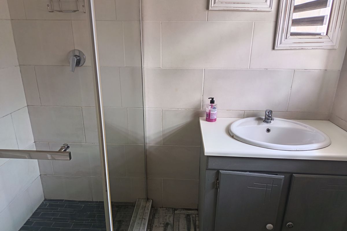 A functional bathroom featuring a glass-enclosed shower, a vanity cabinet with a basin, and neutral wall tiling.