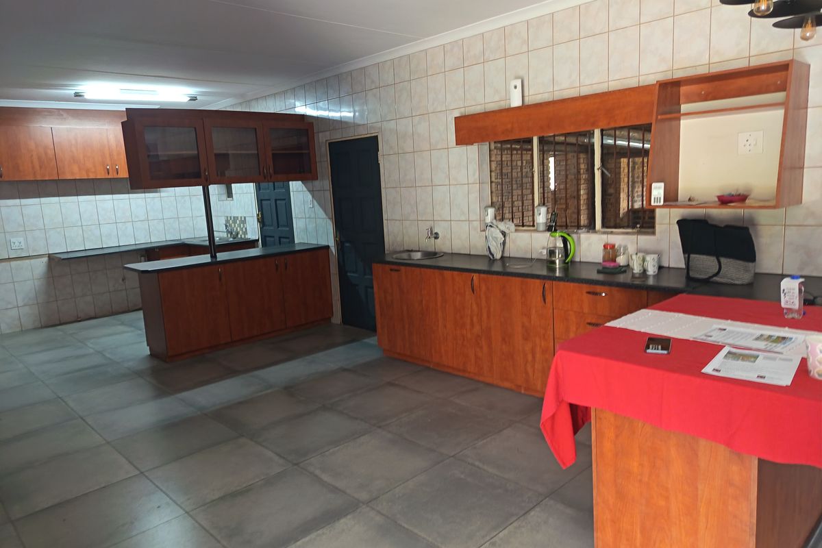 Spacious kitchen featuring extensive wooden cabinetry, tiled backsplash, a central island, and large floor tiles, offering a functional layout with potential for modern updates.