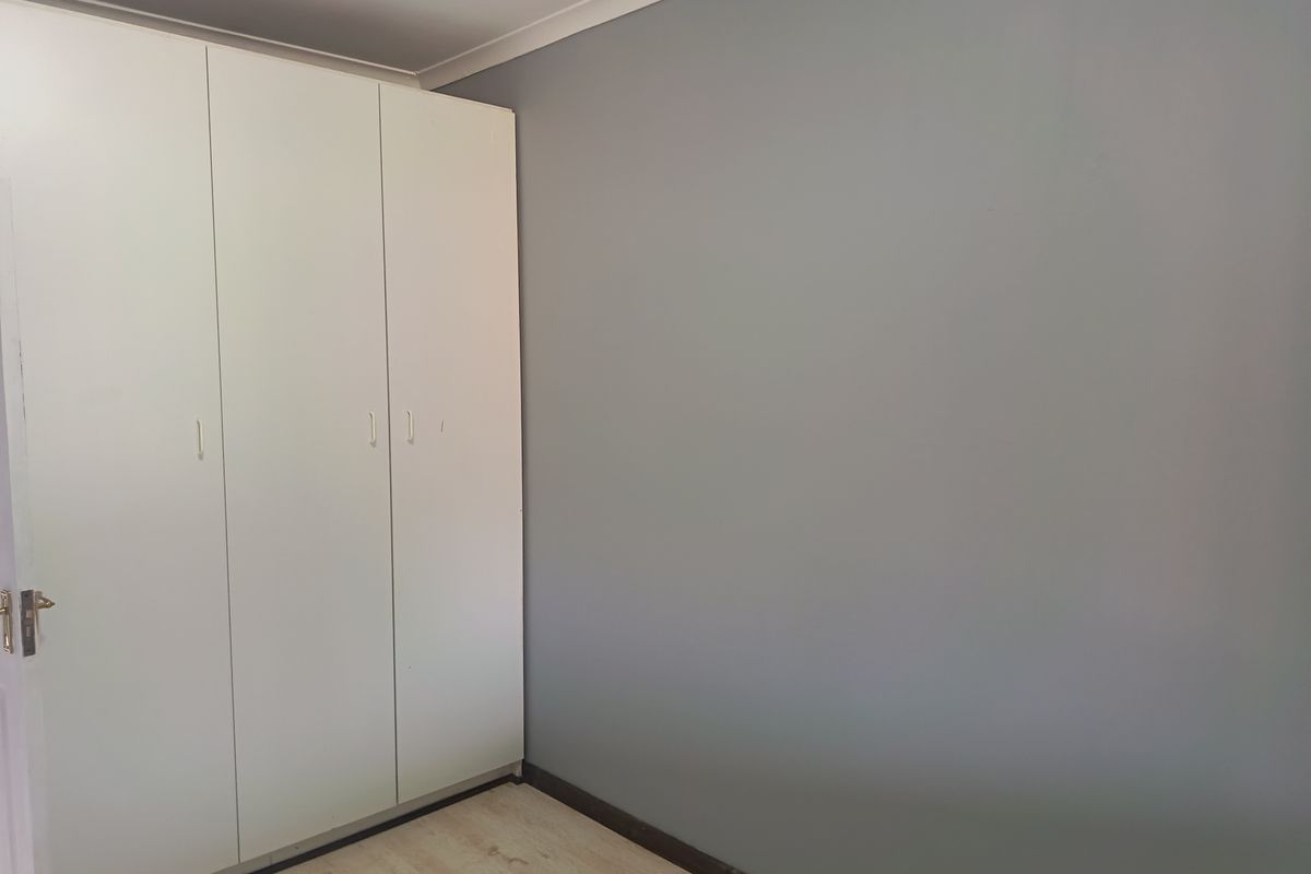 A clean, empty bedroom featuring neutral grey walls, light-toned laminate flooring, and white built-in cupboards with ample storage space.